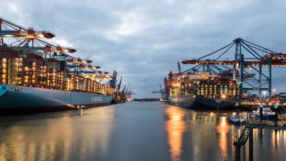 A container terminal working through dusk, cranes lit over the water